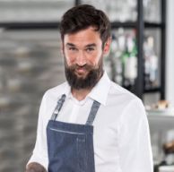 Portrait eines Mannes mit Bart in Restaurant, der weißes Hemd und blaue Schürze trägt