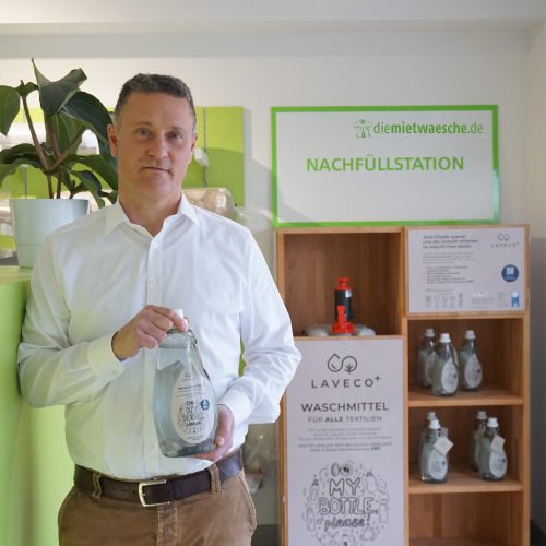 Henrik Rüss hält pflanzliches Waschmittel zum nachhaltigen Abfüllen von diemietwaesche.de