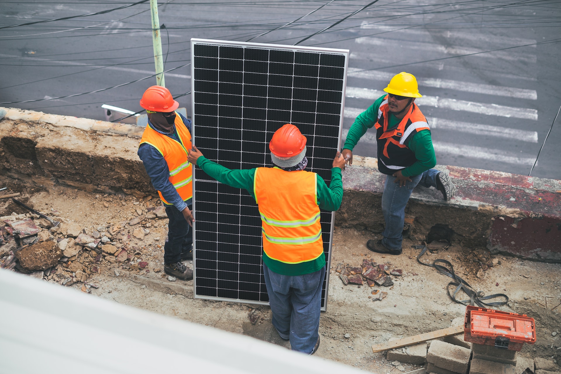 Arbeiter in Warnschutzkleidung, die ein Solarpanel vor sich stehen haben
