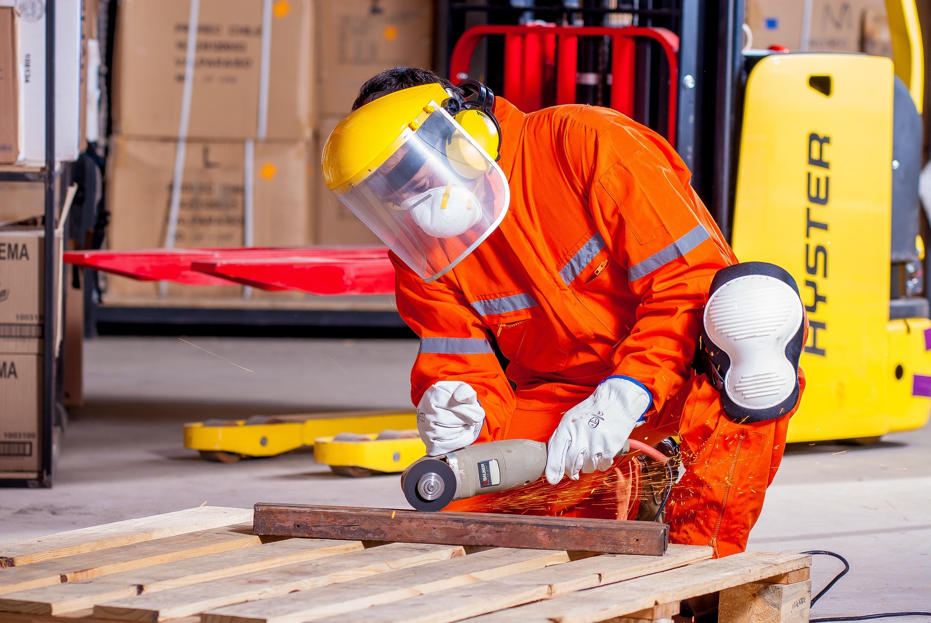 Person in Arbeitsschutzkleidung, Gehör- und Sichtschutz wie auch Mundmaske, die Metall flext