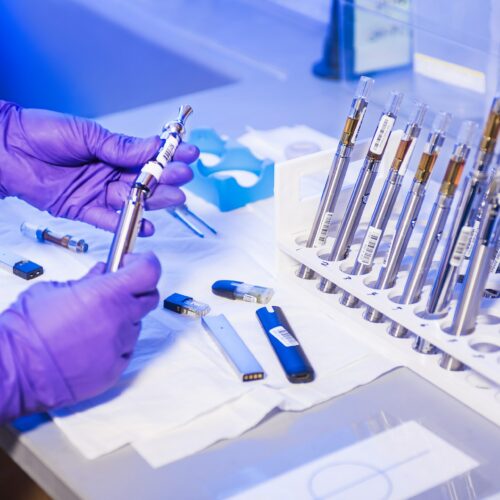 Person, die Schutzanzug und Handschuhe trägt und mit Vapes an einem Tisch arbeitet