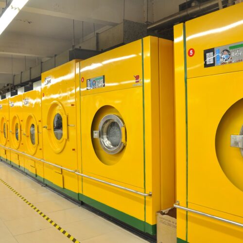 Reihe von großen gewerblichen gelben Waschmaschinen in einer industriellen Wäscherei.