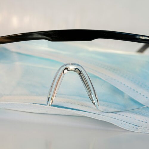 Schutzbrille liegt auf einer chirurgischen Maske auf einem weißen Untergrund.